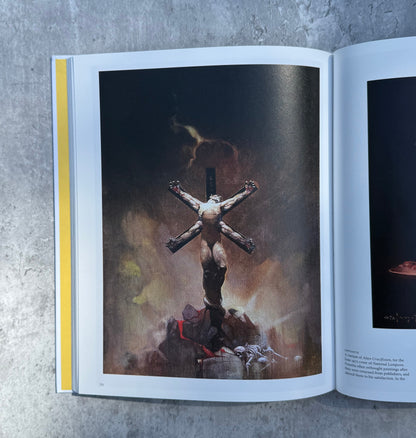 Open book on a textured surface with a photograph of Frank Frazetta artwork. 